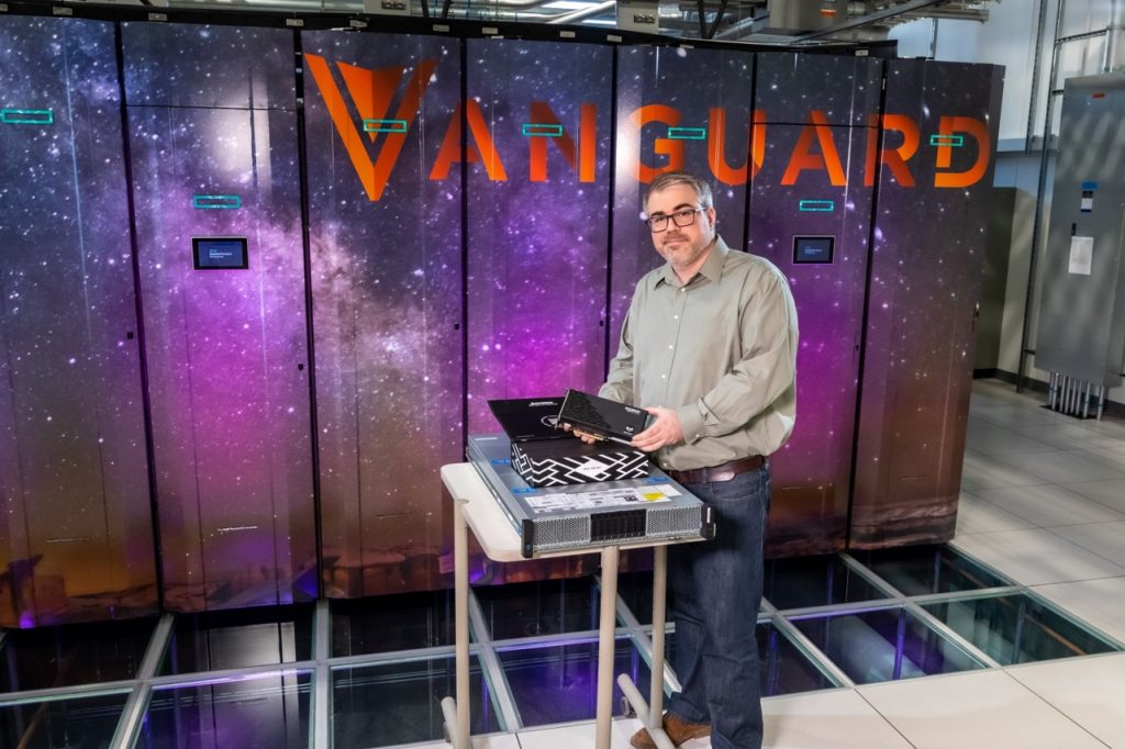 A man holding a prototype system stands in front of the Vanguard supercomputer