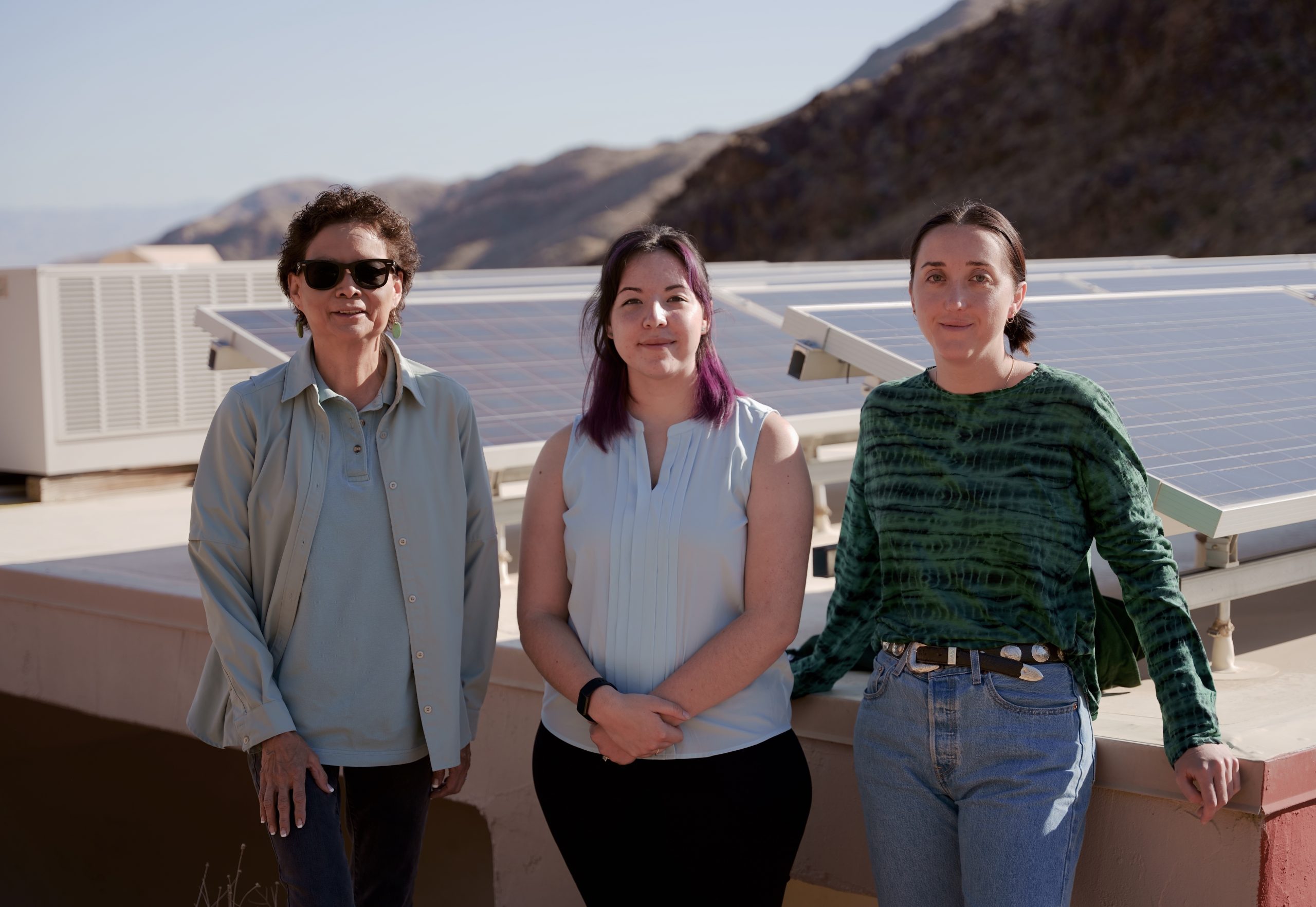 Three women standing in front of solar panels