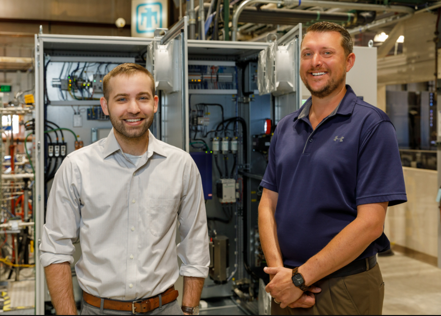 "Two men stand before a cabinet of power system controllers"