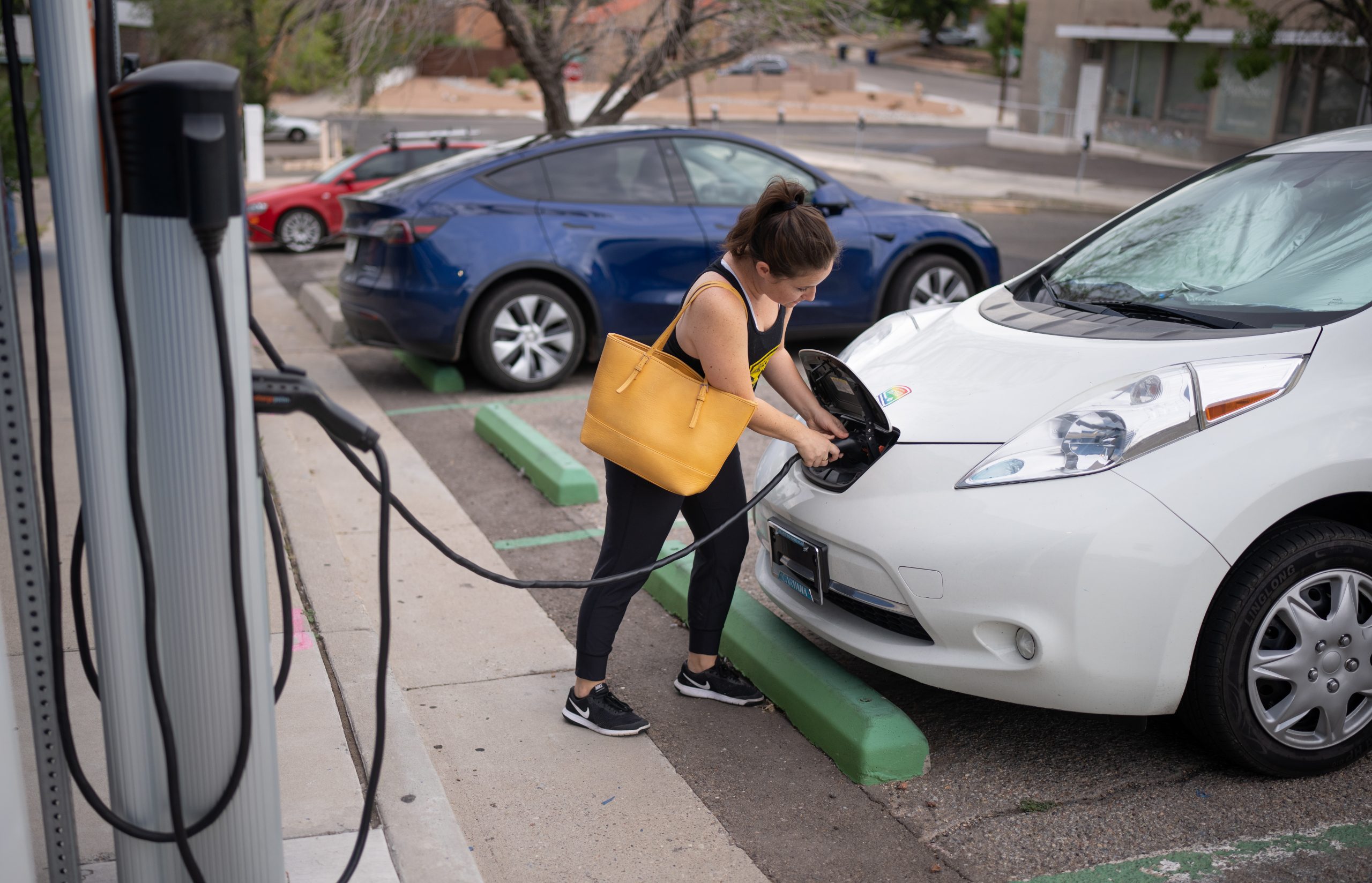 Kaedi Sanchez plugs in her car at a City of Albuquerque electric vehicle charger before heading to work. Sandia National Laboratories researchers have been studying the vulnerabilities of electric vehicle charging infrastructure, including public chargers, to better inform policymakers. (Photo by Craig Fritz)