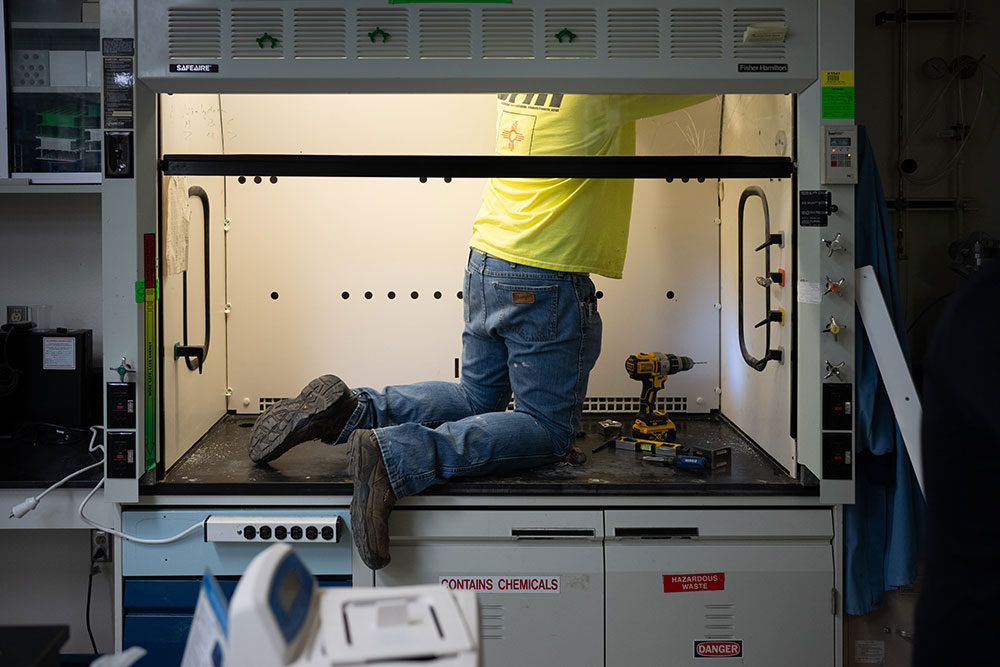 A person kneels while working inside a lab hood