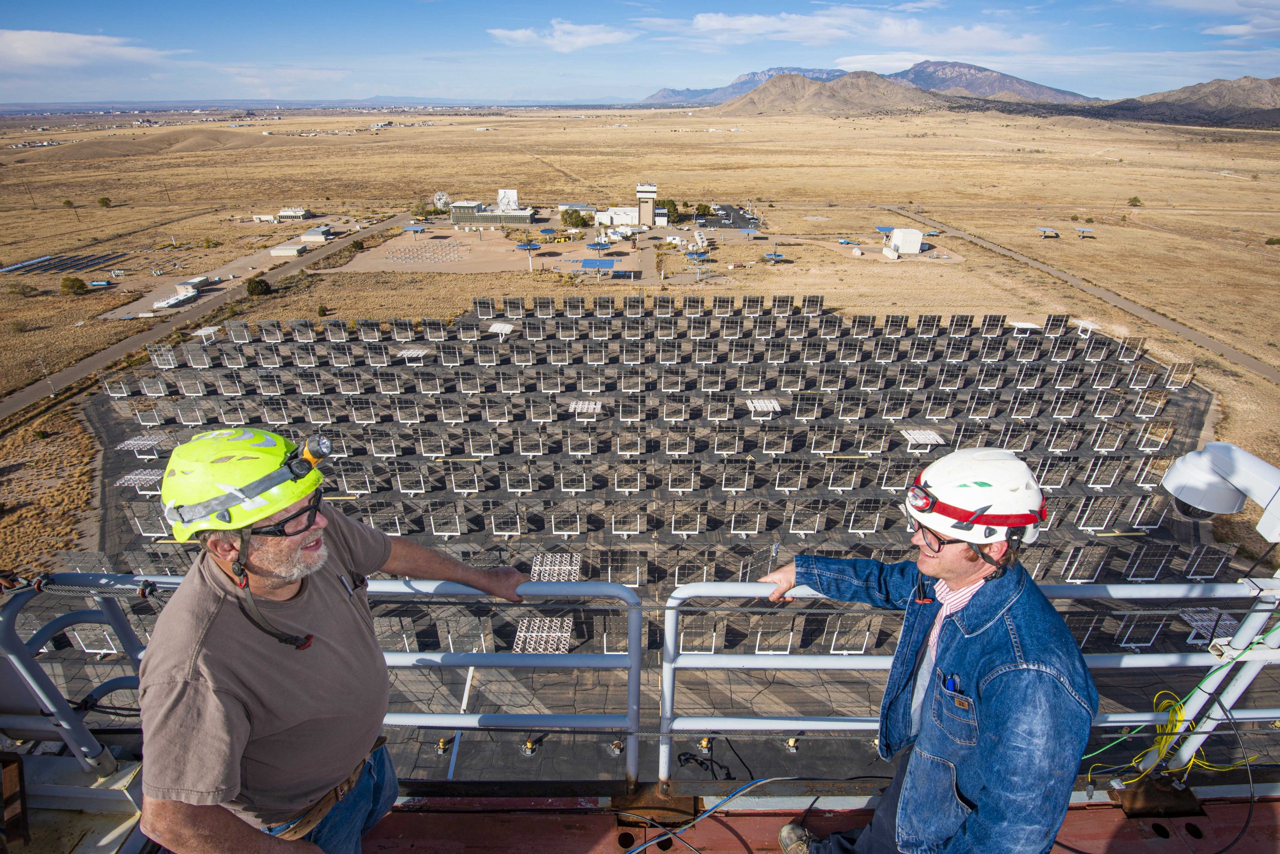 Two technologist stand atop the solar tower with the helioststa and control room behind them