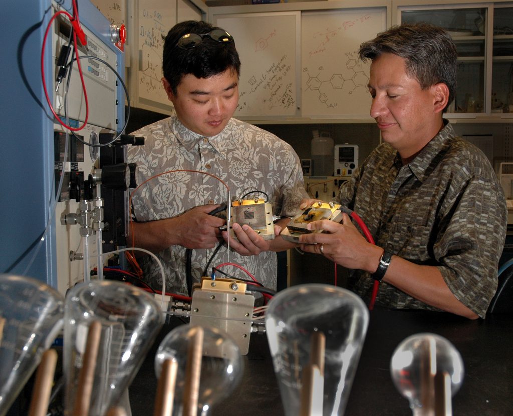 SANDIA RESEARCHERS Cy Fujimoto, left, and Chris Cornelius hold a test micro fuel cell with the Sandia membrane. Next to Fujimoto is a micro fuel test station.