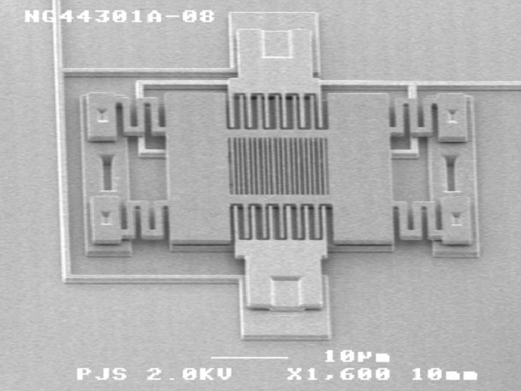 SEM (scanning electron micrograph) of the device, with scale bar at bottom representing 10 microns. The top grating layer is suspended by 4 springs and actuated by two side comb drives. The second, fixed grating layer is hidden below the first. The area of the grating itself is 10 microns x 10 microns.Download 300dpi JPEG image, ‘device.jpg’, 168K (Media are welcome to download/publish this image with related news stories.)