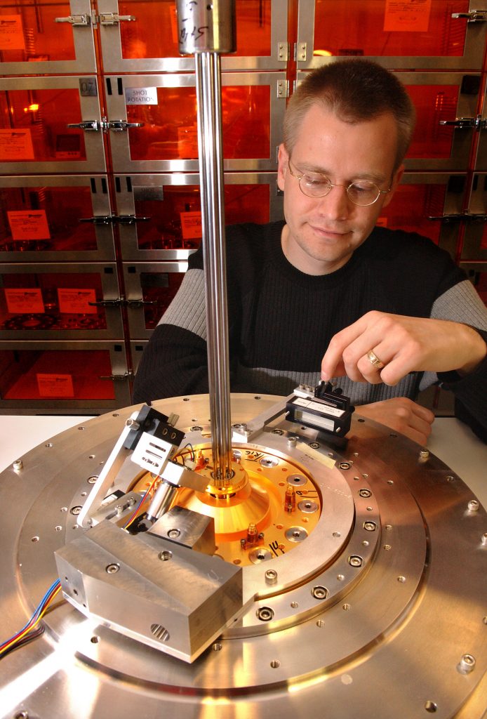 Sandia National Laboratories researcher Daniel Sinars demonstrates the setup he and his team created to peer into the center of Sandia’s Z machine at the moment of firing. The crystal under his finger is attached to portions of a Z target configuration.