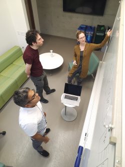 Three people study a whiteboard