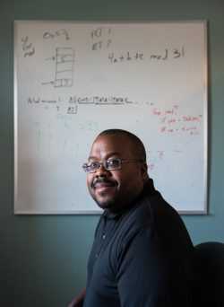 A man poses in front of a whiteboard filled with sketches and notes