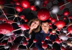 Man and woman look through a network of red, grey and gold balls.