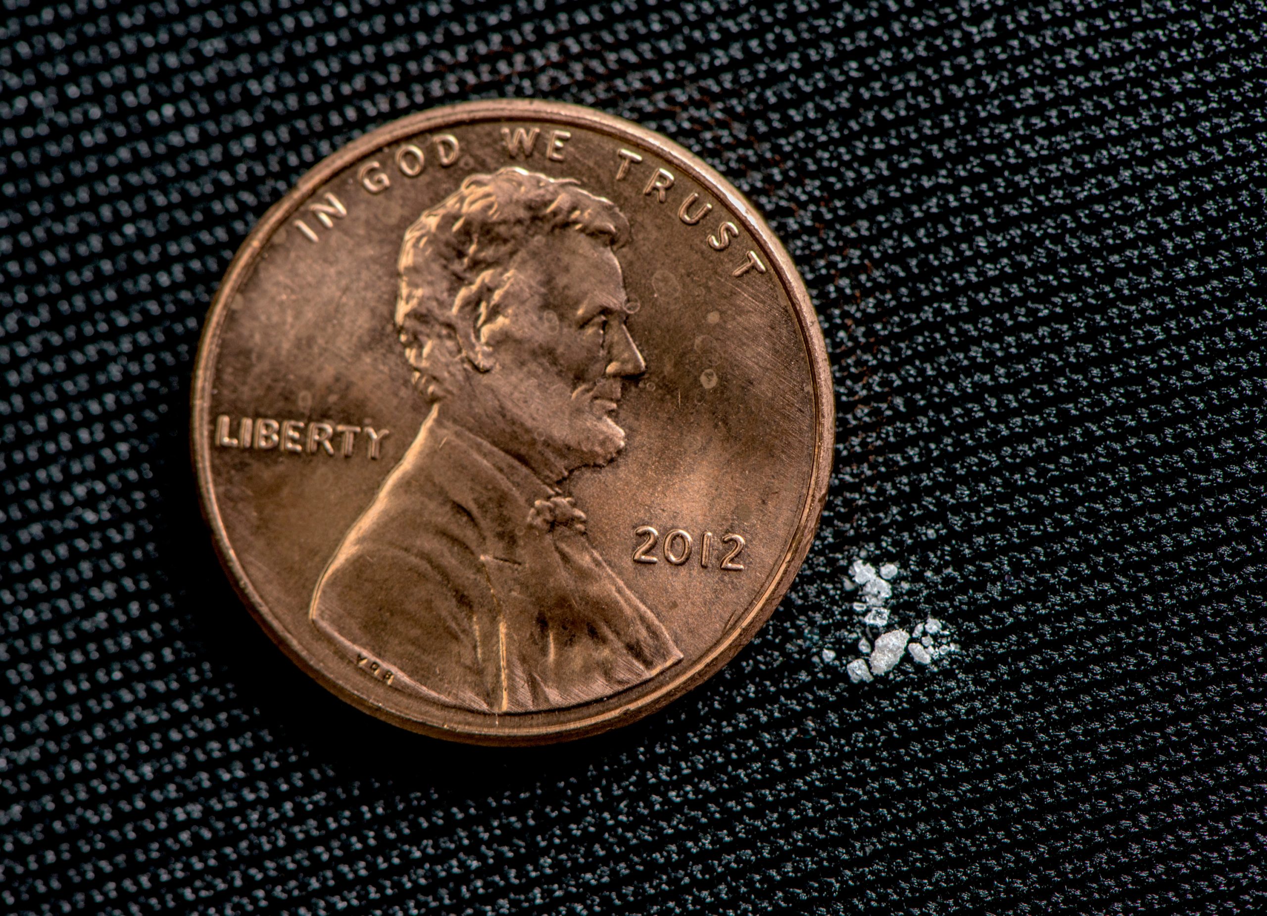 A U.S. Penny on a black background next to a few small white grains.