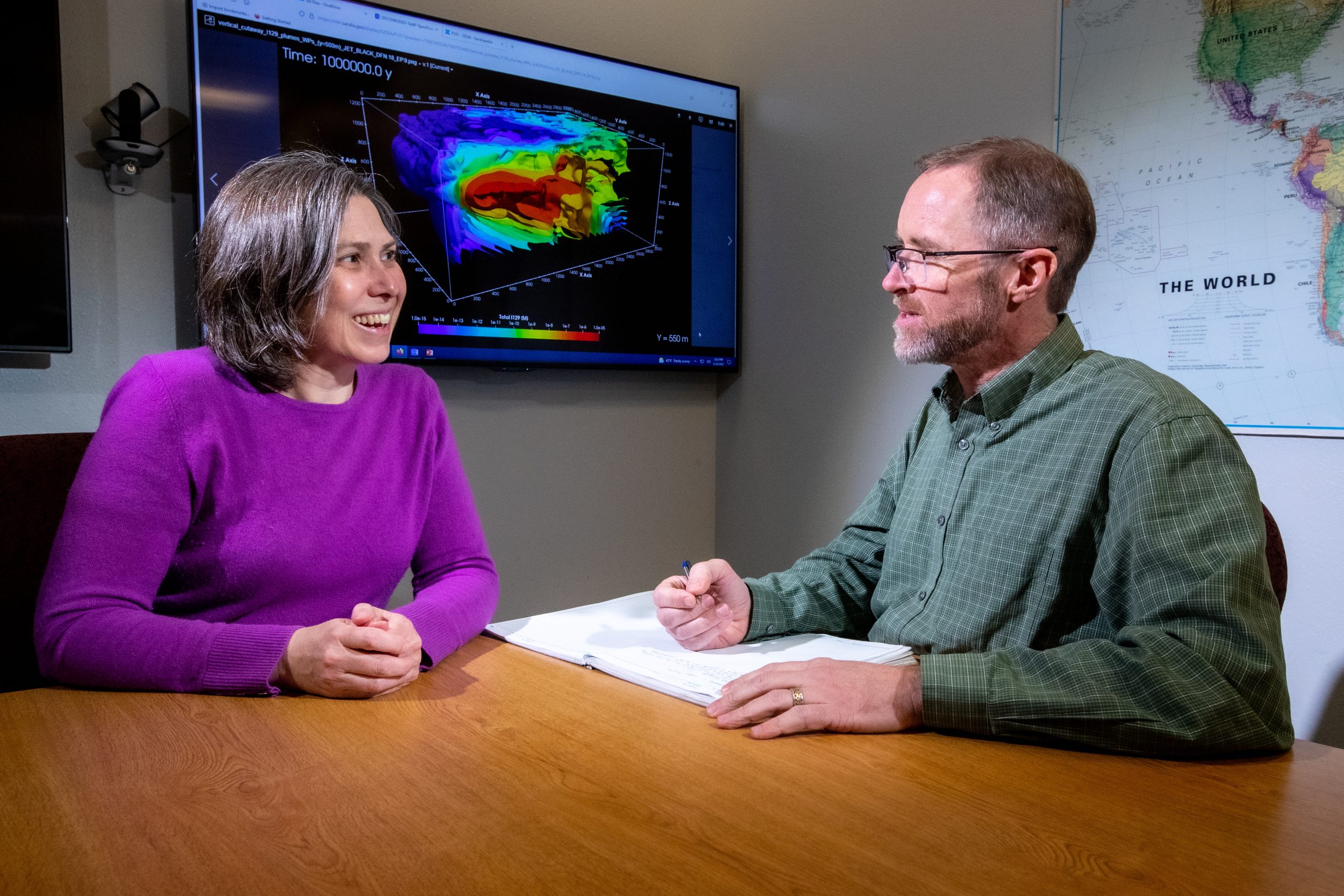 Woman and man talk with a colorful computer model on a screen behind them.