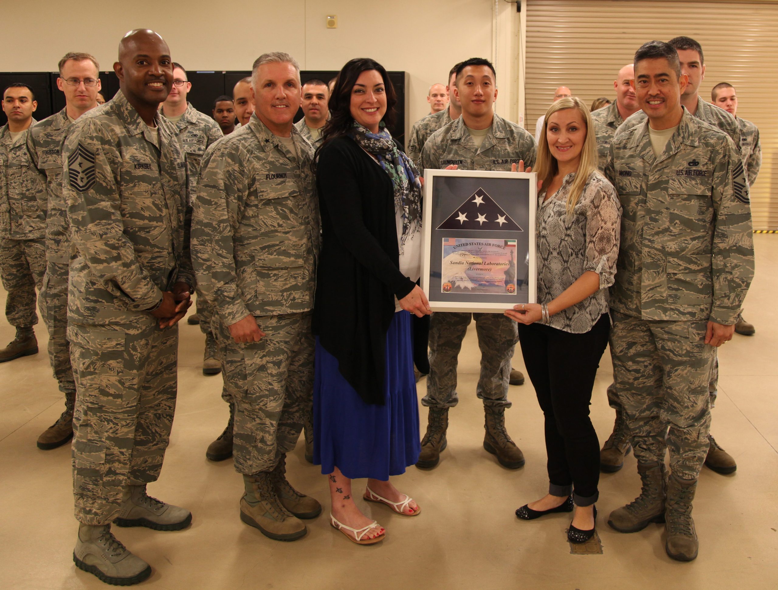 Brig. Gen. John C. Flournoy Jr., second from left, presents a U.S. flag to Heather Egtervanwissekerke, to the left of the flag, and Michele Clark of Sandia National Laboratories' Military Support Committee at the 945th Aircraft Maintenance Squadron, Travis AFB.