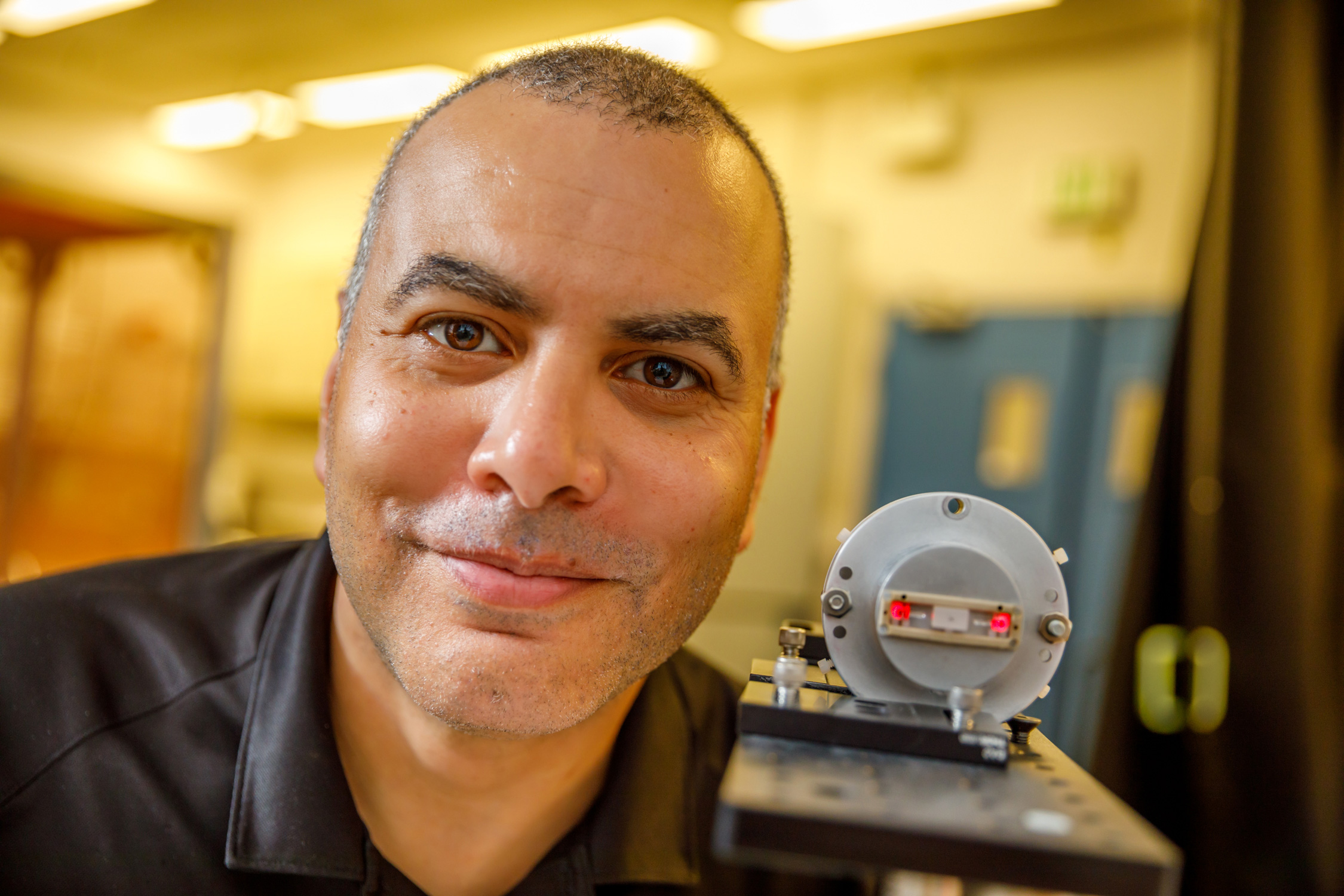 Sandia National Laboratories researcher Israel Owens holds the optical sensor used to house the crystal that proved central to his team’s successful attempts to measure very high voltages. The two red spots on each side of the crystal are due to laser light reflecting off the side mirrors used to direct light through the middle of the crystal. The actual experiments used green laser light.