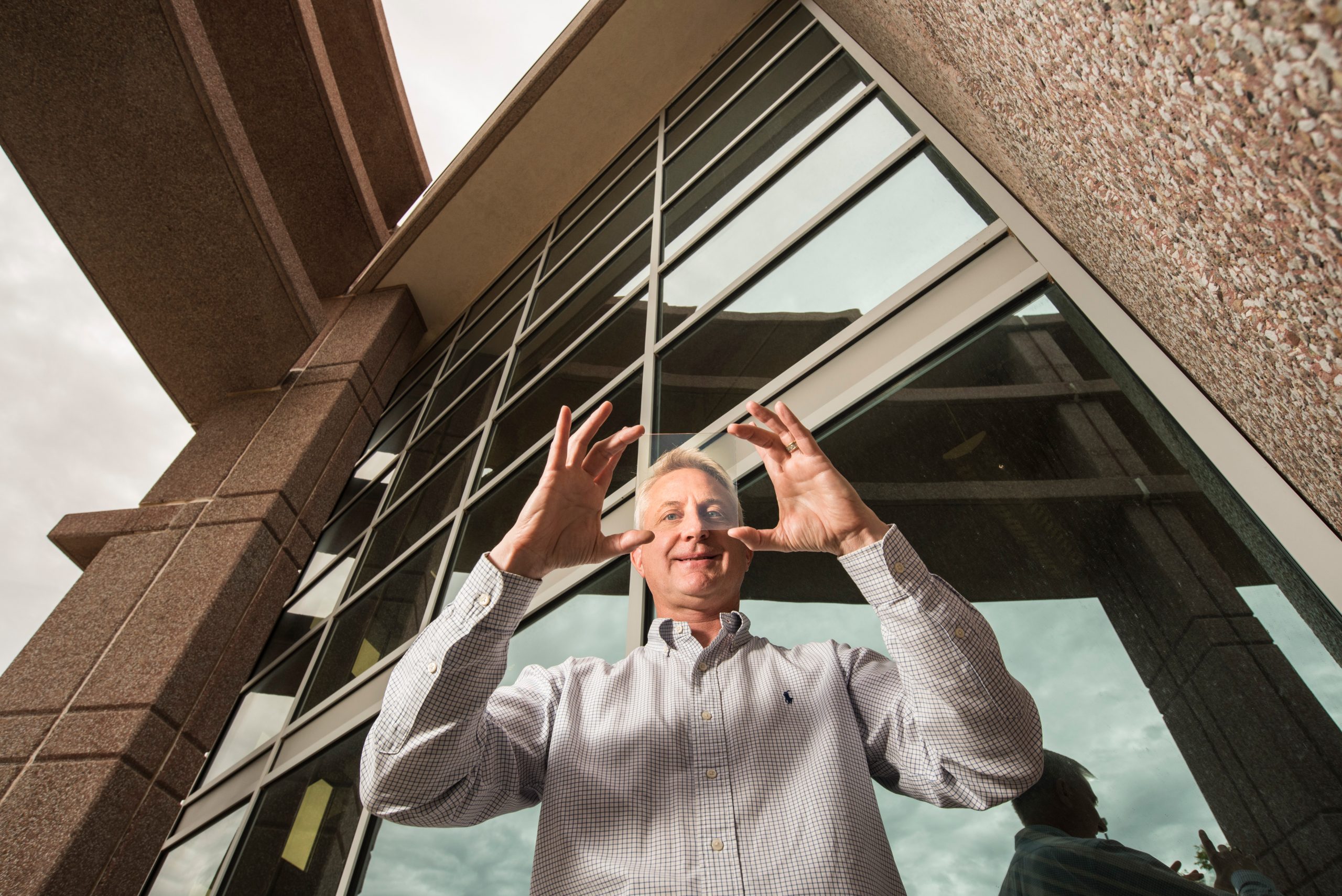 Materials physicist Paul Clem holds a sample of nanoparticle coated glass in front of an office building.