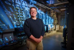 Michael Ropp in Sandia’s Distributed Energy Technologies Laboratory with binary code displayed behind him.