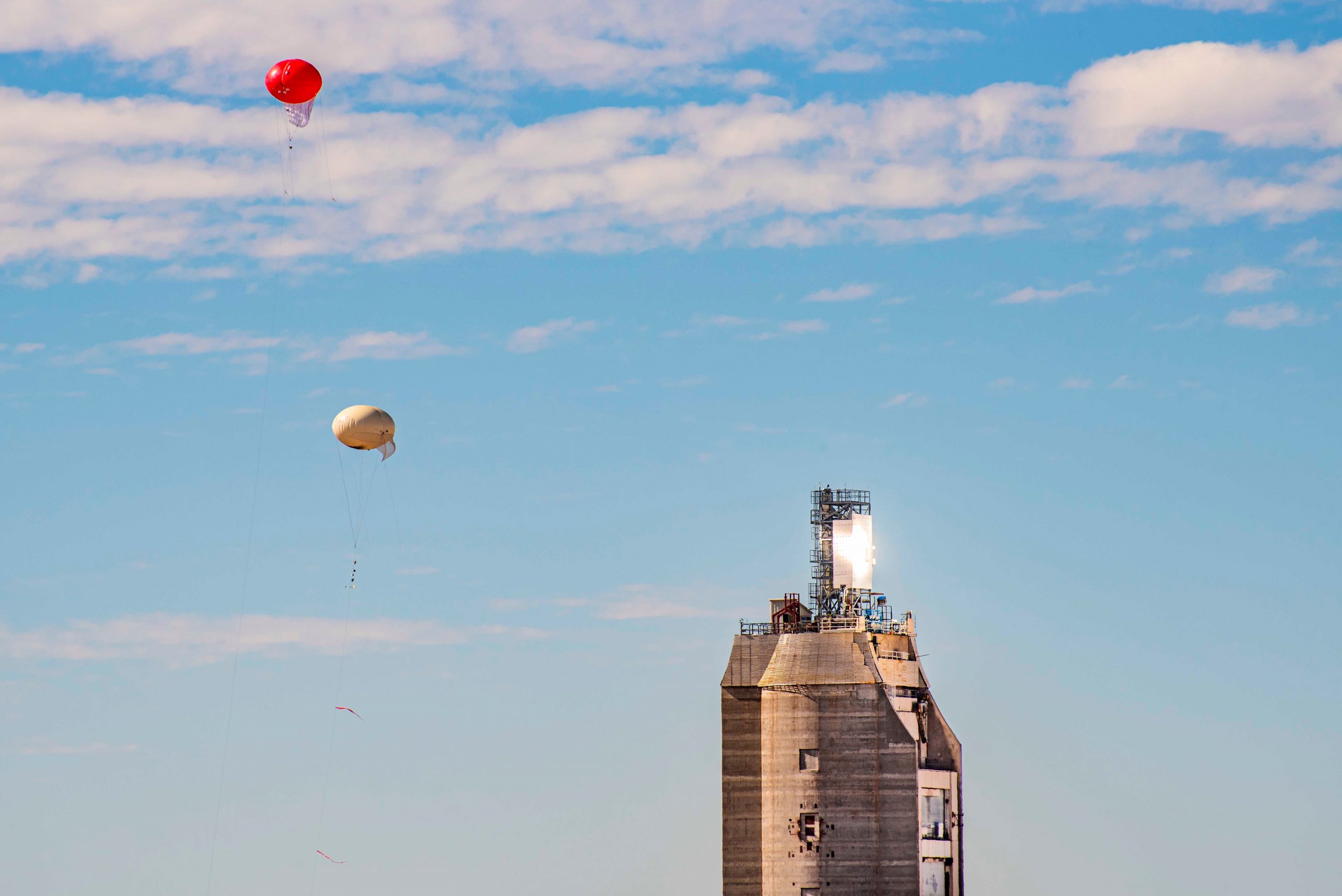 Two small balloons against a blue sky to the left of a large tower with a