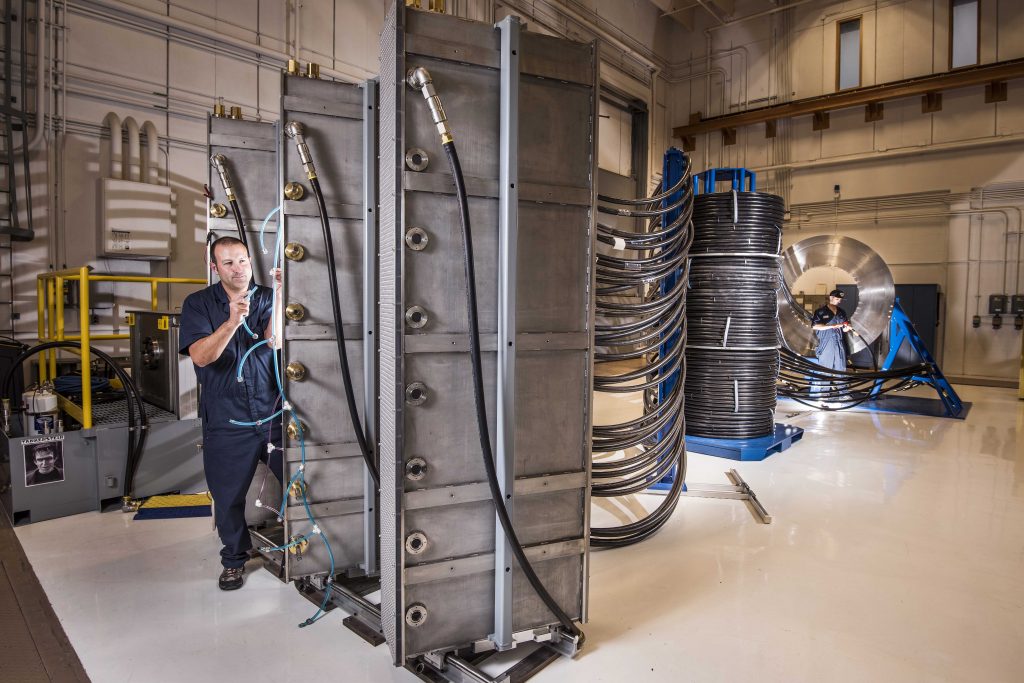 Sandia National Laboratories technician Tommy Mulville installs a gas exhaust line for a switch at Thor’s brick tower racks. In the background, beyond the intermediate support towers, technician Eric Breden makes ready an electrical cable for insertion in the central power flow assembly. (Photo by Randy Montoya) Click on the thumbnail for a high-resolution image.