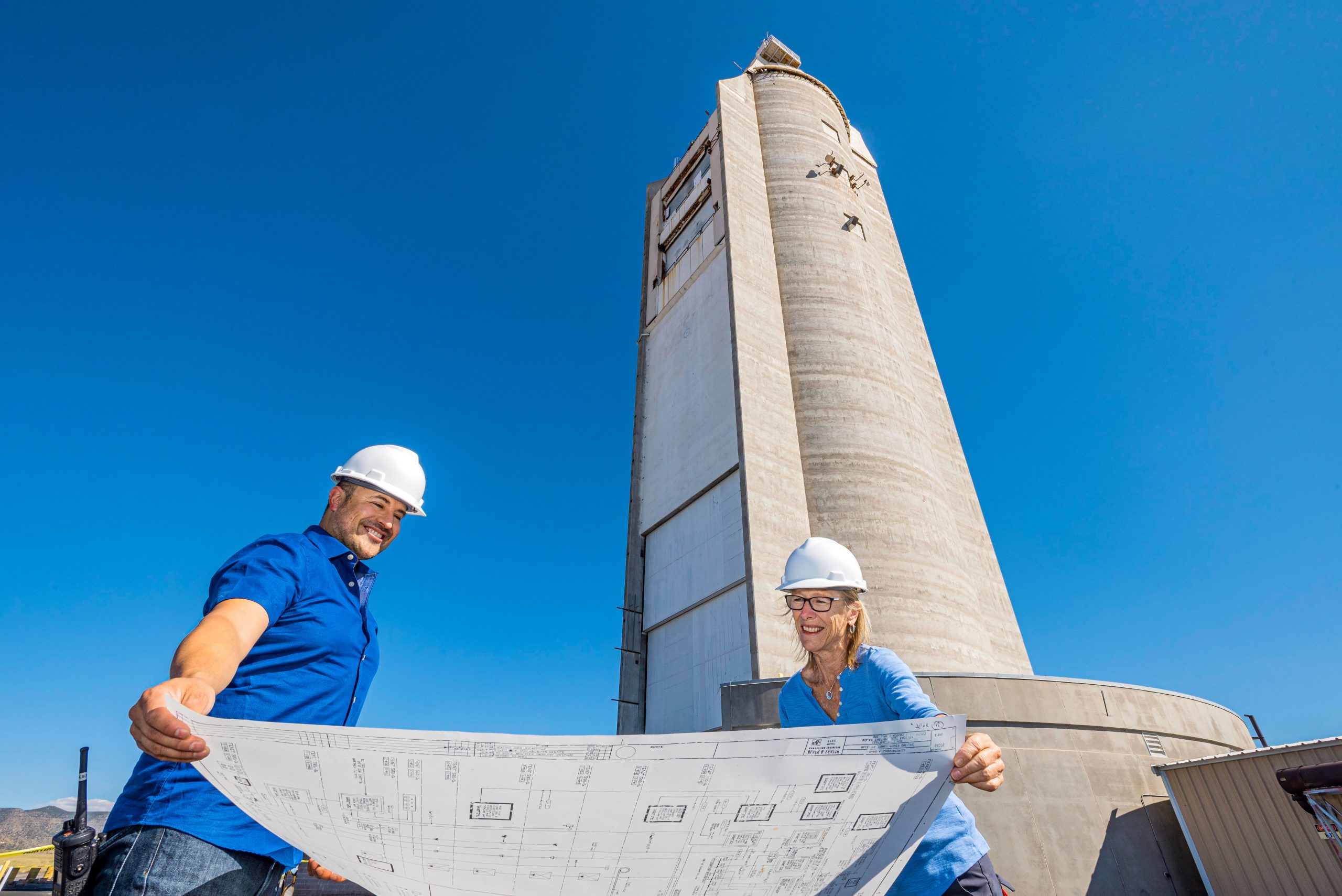 Two people look at blueprints with Sandia's Solar Tower looming large above.