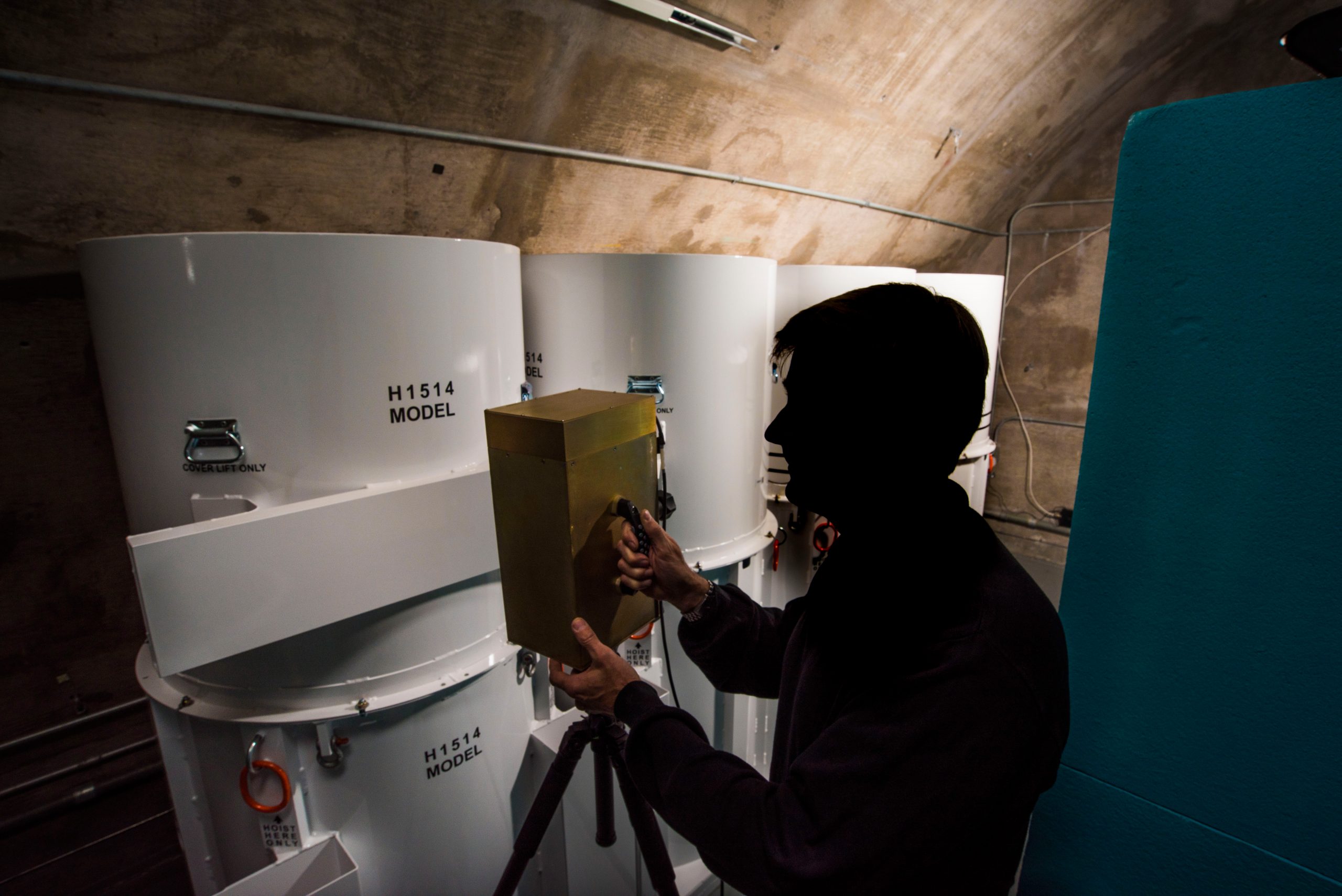 A man in profile scans three white canisters with a brass box -- the new neutron detection equipment