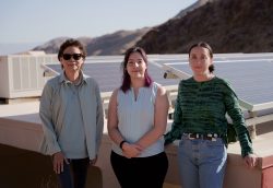 Three women standing in front of solar panels.