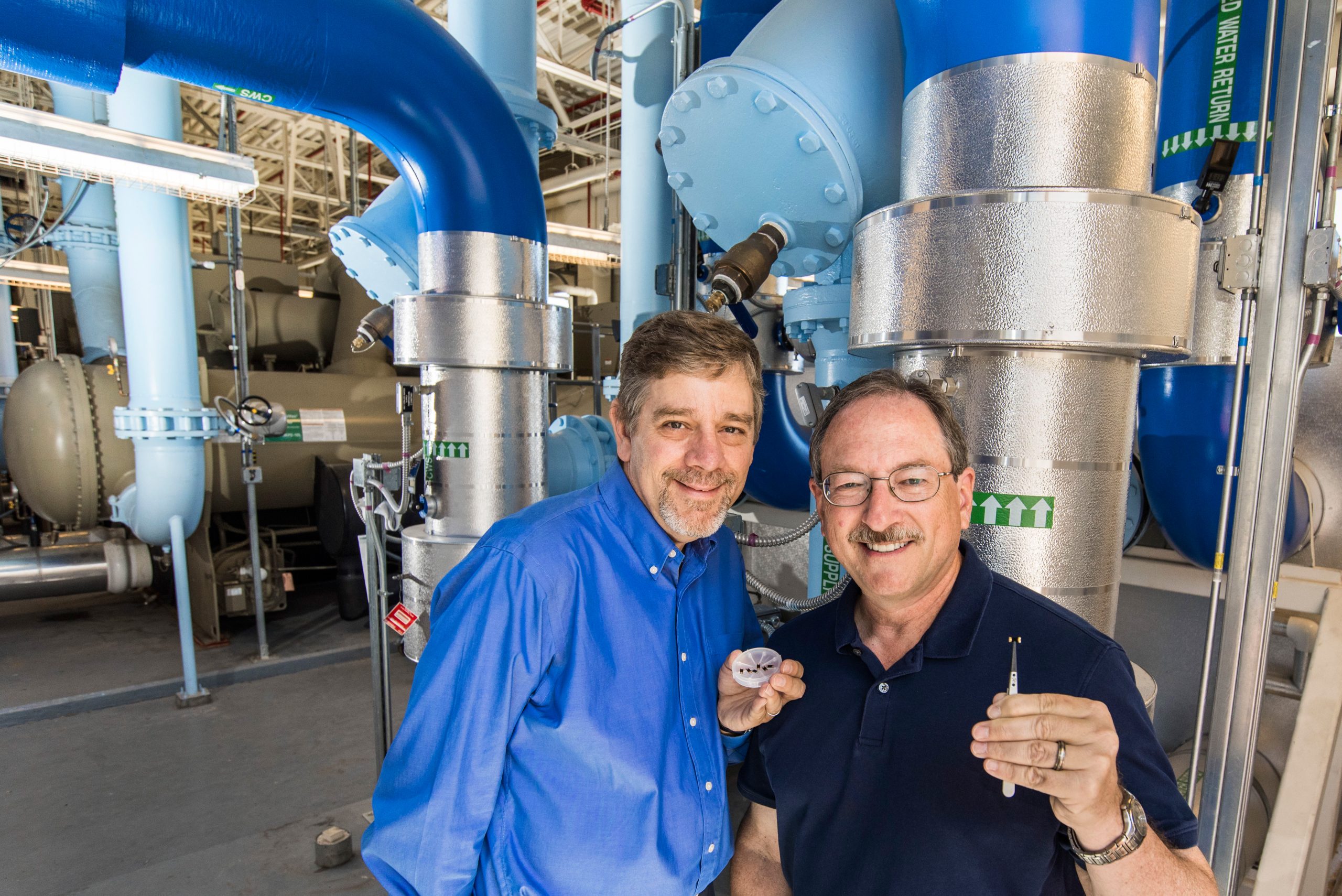 Curtis Mowry and Mike Siegal with tiny nanoporous carbon coated SAW sensors in front of blue water pipes