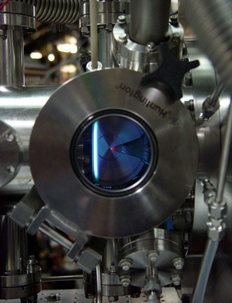 This low-pressure, flame-sampling apparatus shows a rich flame burning in the vacuum chamber. The quartz cone through which flame gases are sampled is visible entering from the right of the apparatus. The tip is glowing because of incandescence of soot deposits on the cone. The burner is on the left; it can be moved horizontally so that gases are sampled from different positions in the flame.