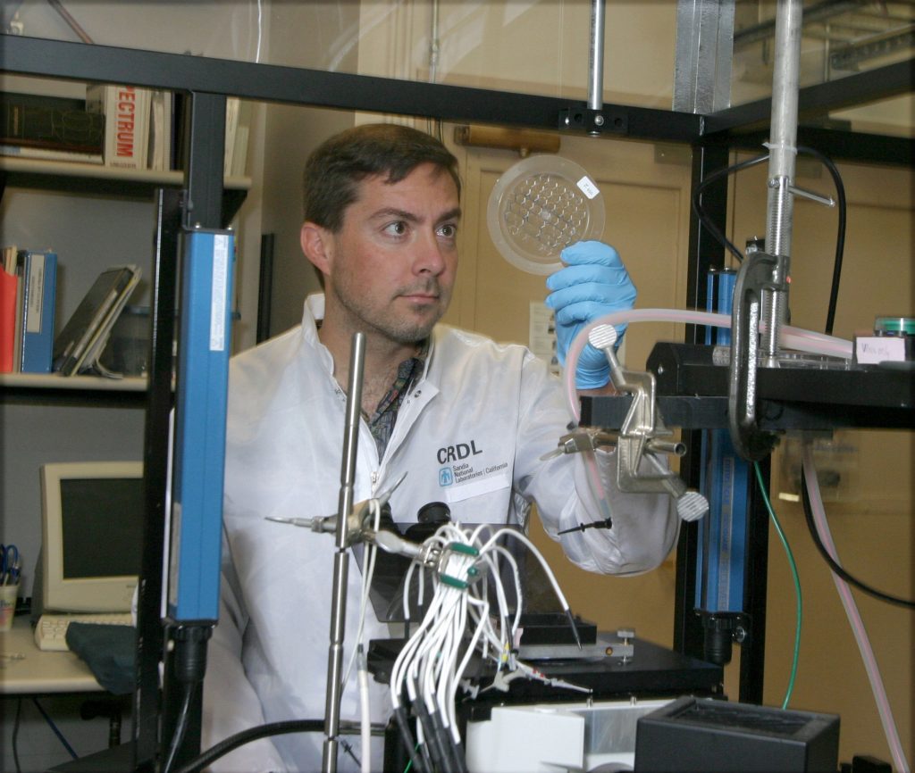 Sandia’s Eric Cummings visually inspects an iDEP device for proper alignment before evaluating it with a fluorescent microscope. Among other potential applications, iDEP may allow for protein isolation and concentration, sample concentration and focusing, analytical chemistry, and mass spectrometry for proteomics and drug discovery.