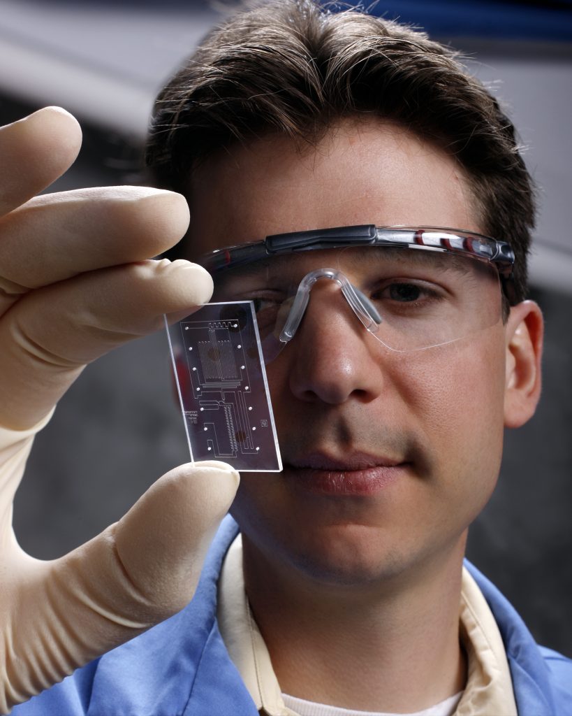 Sandia researcher Thomas Perroud examines a MICA chip. MICA enables researchers to precisely target, sort, and measure samples as small as a single cell in an automated system that includes flow cytometry (Photo by Randy Wong). Download 300dpi 3.99MB JPEG image (Media are welcome to download/publish this image with related news stories.)