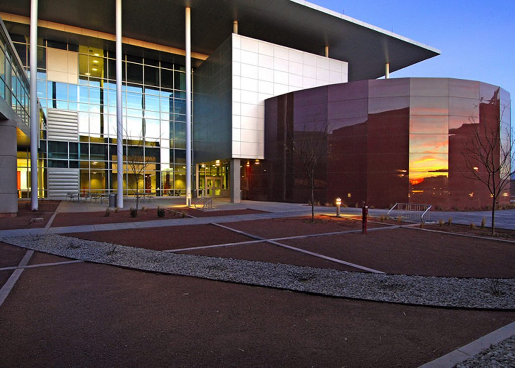 The setting sun reflects off the glass of the cylindrical training center attached to Sandia’s new MicroLab building. The building is the second of three to come online of the defense lab’s $500 million MESA project.