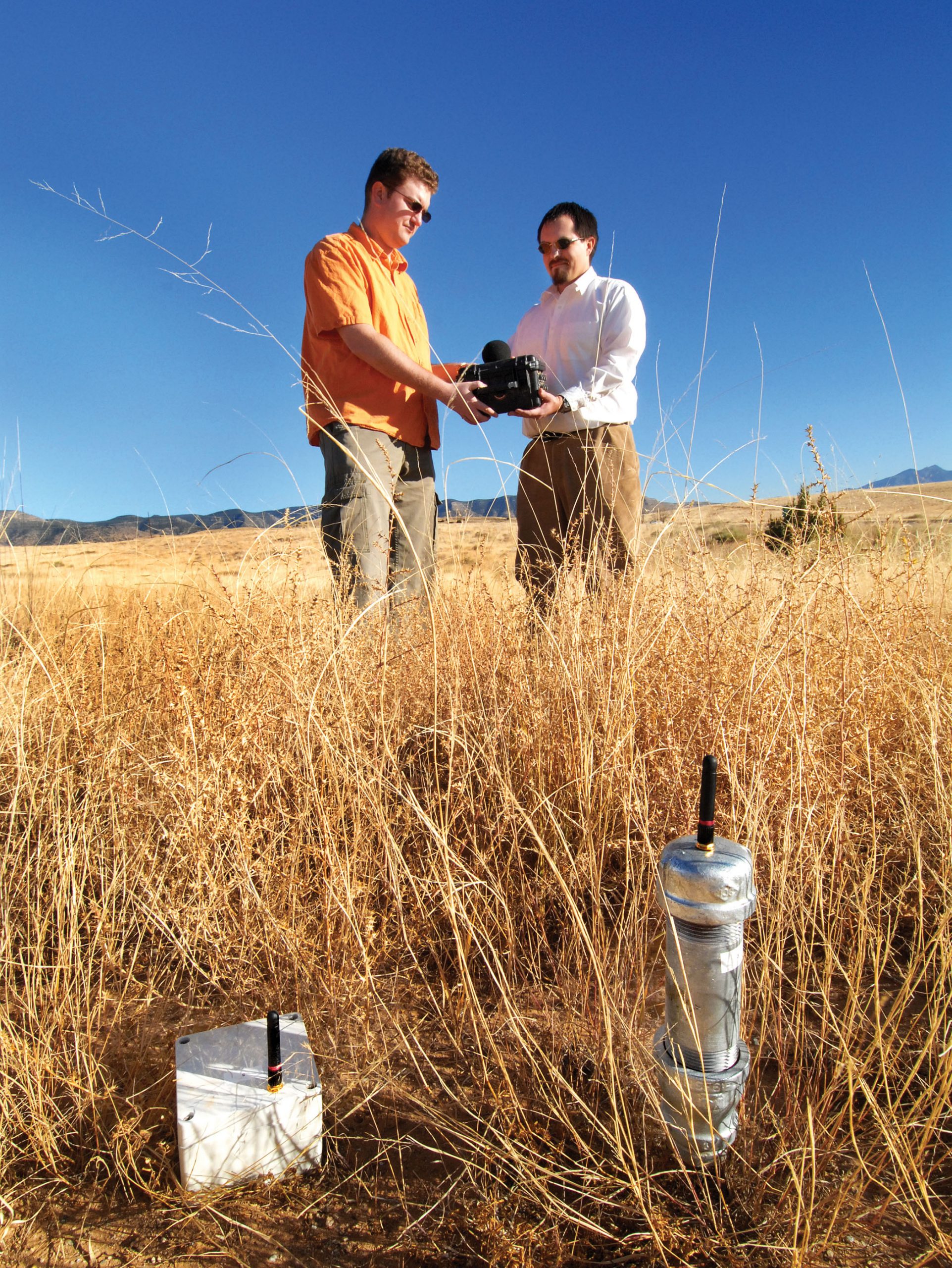 Sandia researchers Jonathan Van Houten (left) and Jeremy Giron hold a Labs-designed sophisticated sensor that interacts with smaller off-the-shelf sensors like those seen in the foreground.