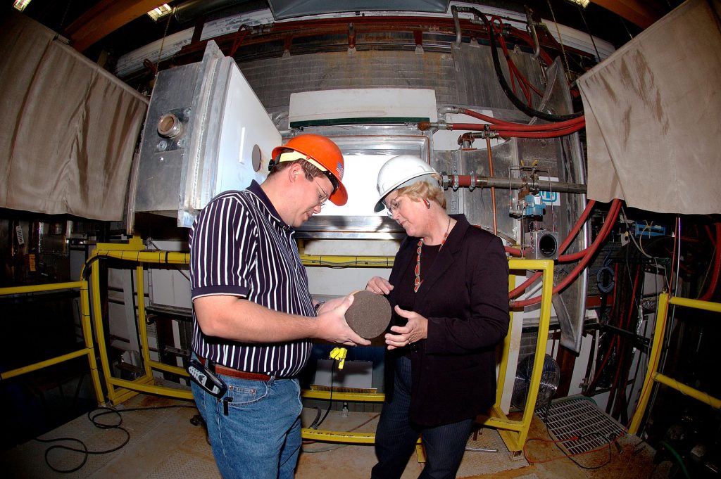 Sandia’s Cheryl Ghanbari and Steve Moon of Gray Research, look at a 5-inch-diameter ablator sample that was tested in Sandia's solar wind tunnel.