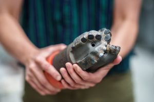 A close-up of a woman holding a large drill bit. It looks somewhat like a molar with many flat facets.