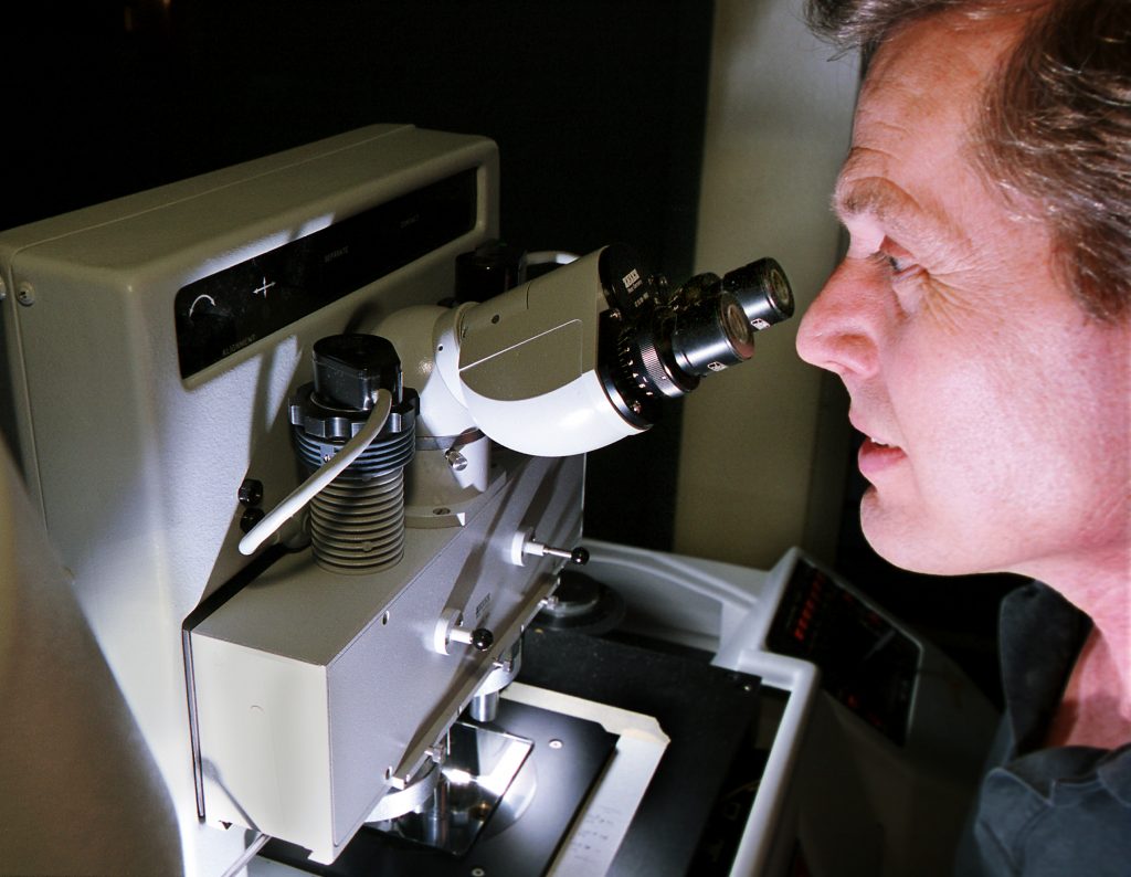 SANDIA RESEARCHER Paul Gourley examines the photomask used to microfabricate the biocavity microlaser flow device.