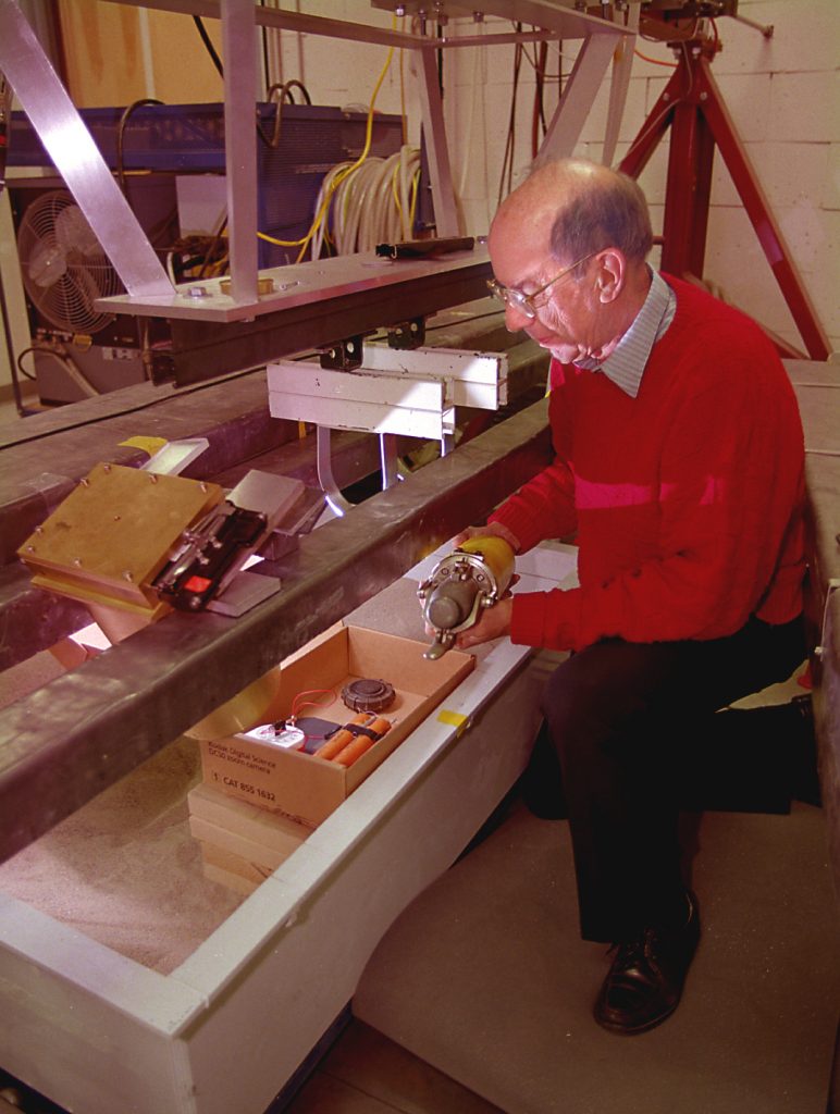 SOMETHING WRONG WITH THAT PACKAGE -- Sandia researcher Grant Lockwood holds a laboratory version of his off-the-shelf X-ray source to safely examine the insides of containers that could conceal bombs. Shown in the already opened box are two simulated sticks of dynamite, a timer, and a detonator.