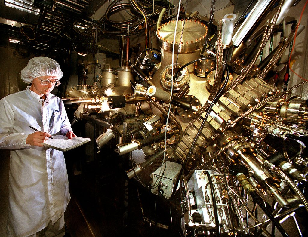 CRYSTAL GROWTH -- Sandia researcher John Klem stands next to the molecular beam epitaxy system used to grow the crystal structure of the 1.3-micron communications vertical cavity surface emitting laser (VCSEL).