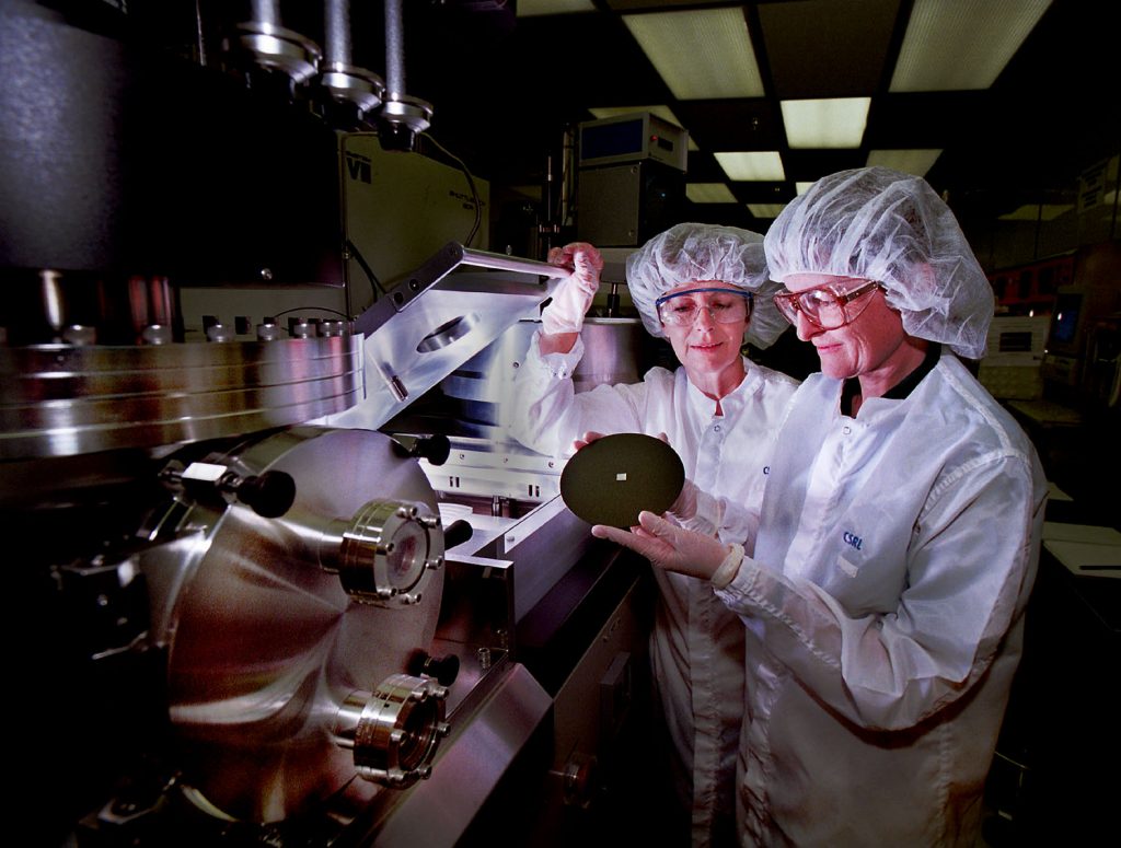 Sandia researchers Carol Ashby (foreground) and Carolyn Matzke prepare to put a wafer sample into a high-density plasma chamber used to deposit thin films on wafers. At the center of the wafer is a thumbnail-sized chip laden with the makings of tiny fluidic canals.