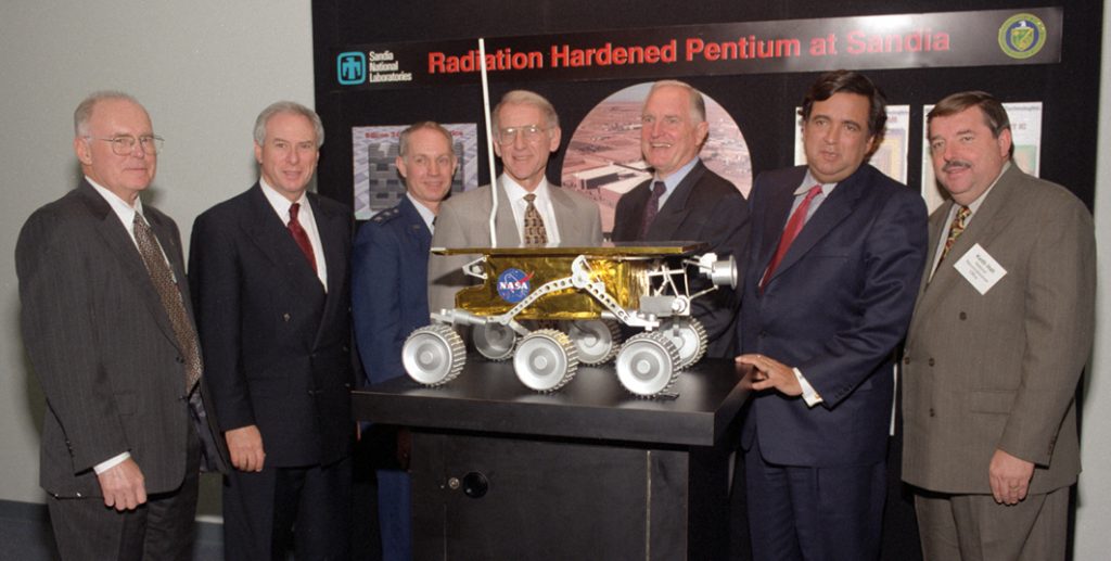 The Dec. 8 announcement at Intel headquarters that the giant chip-maker is transferring its Pentium chip at no fee to Sandia to redesign into a radiation-hardened version for military and space applications involved an impressive gathering. From left are Intel co-founder and Chairman Emeritus Gordon Moore, NASA Administrator Dan Goldin, Air Force Research Laboratory Commander Maj. Gen. Dick Paul, Sandia Executive VP John Crawford, Intel President and CEO Craig Barrett, Secretary of Energy Bill Richardson, and National Reconnaissance Office Director Keith Hall. A full-scale model of the Soujurner rover, used during NASA's July 1997 Mars Pathfinder mission, is in the foreground. The rover contains an earlier-generation Intel chip that Sandia redesigned into a radiation-hardened version. (Sandia photo by Randy Wong)Download 150dpi JPEG image, 'rover.jpg', 544K