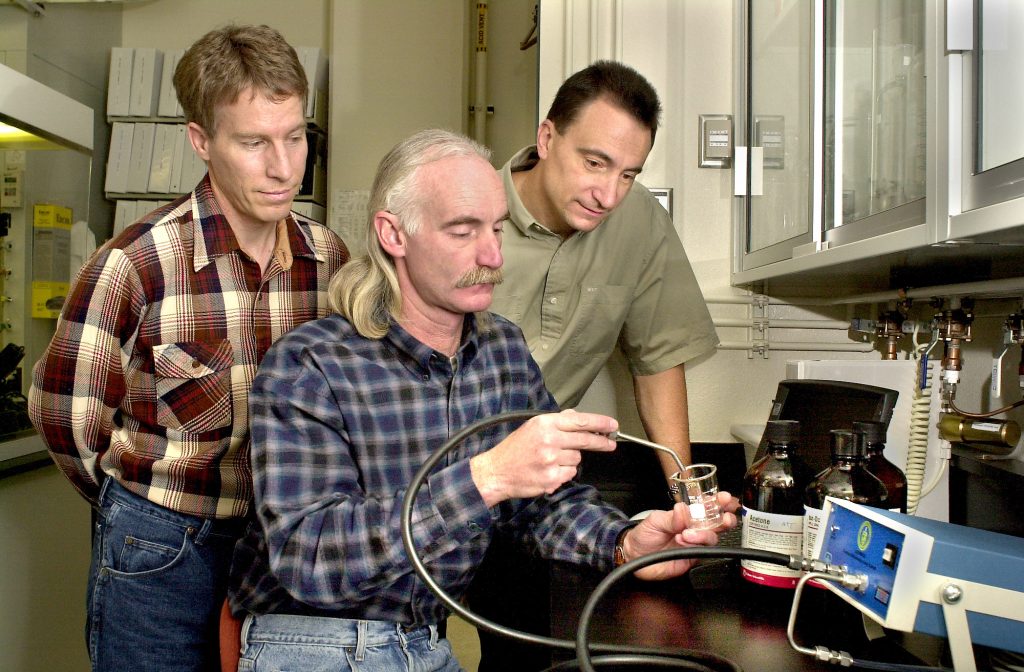 READY FOR FIELD TESTING — Sandia researchers Graham Yelton (left) and Richard Cernosek (right) watch as Alan Staton conducts a lab test using Sandia's lightweight portable chemical vapor detection system. It is now being refined in preparation for field testing in a chemical plume in 2001.