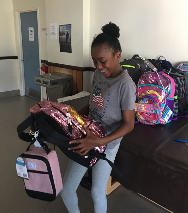 GLITTERY BACK-TO-SCHOOL — A Camp Parks child can hardly contain her excitement for her new backpack. Back to school season represents a financial burden for Bay Area military families with the region's high cost of living.