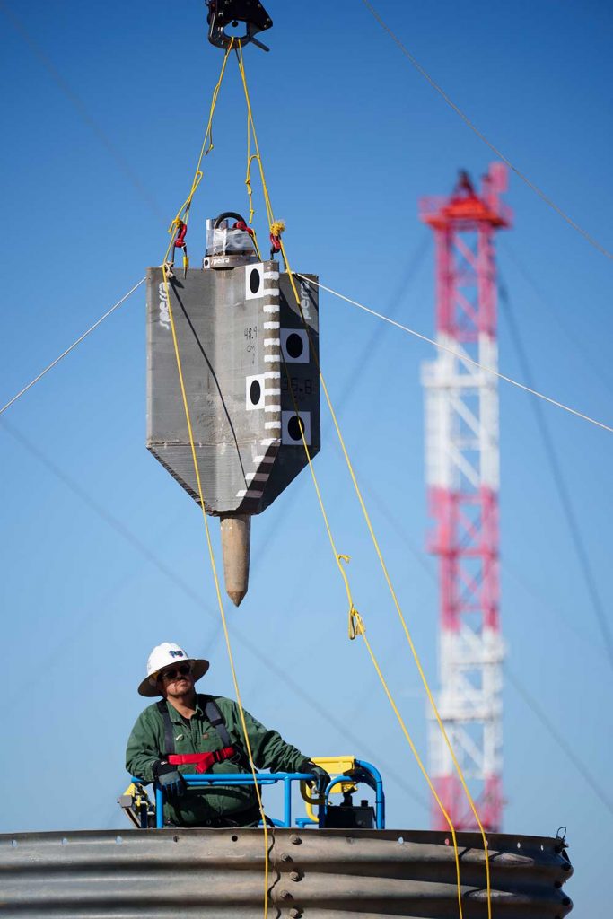 READY TO DROP — Technologist Jamie Meza guides a torpedo anchor prototype as it is lifted over a test bed at the Drop Tower facility. The anchor is being tested for use with offshore wind turbines. (Photo by Craig Fritz)